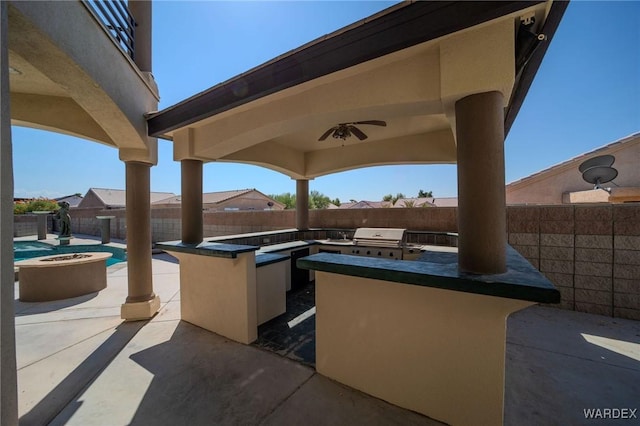 view of patio featuring grilling area, an outdoor kitchen, a ceiling fan, a bar, and a fenced backyard