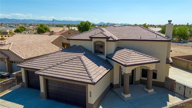 view of front of property with concrete driveway, a tiled roof, fence, a mountain view, and stucco siding