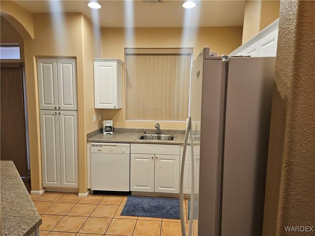 kitchen featuring light tile patterned floors, arched walkways, a sink, freestanding refrigerator, and dishwasher