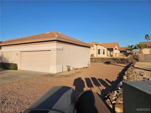 view of side of property with concrete driveway, an attached garage, a tile roof, and stucco siding