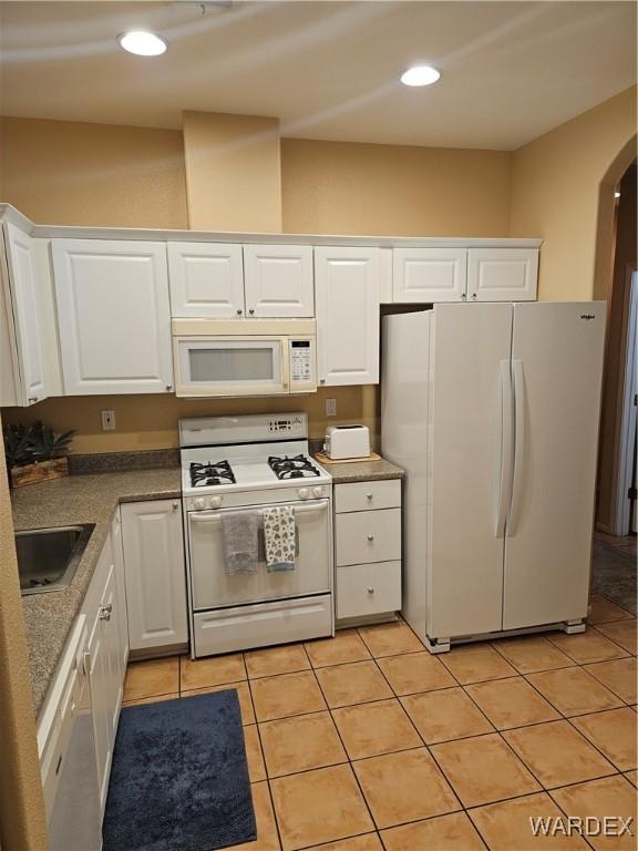 kitchen featuring arched walkways, white appliances, a sink, and white cabinetry