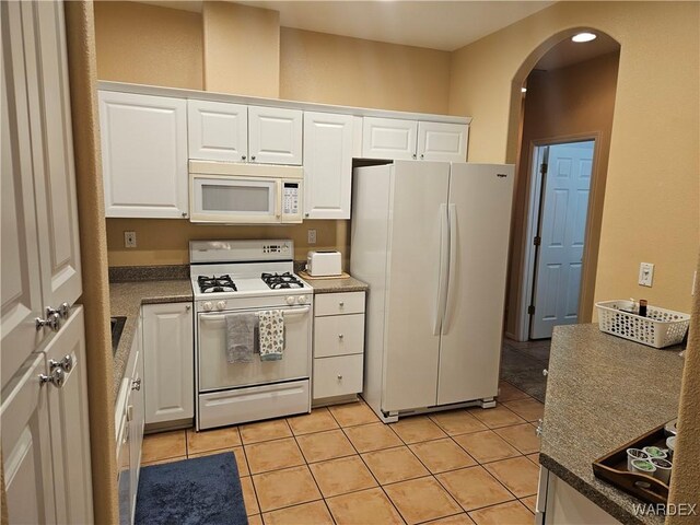 kitchen featuring arched walkways, white appliances, light tile patterned flooring, and white cabinets