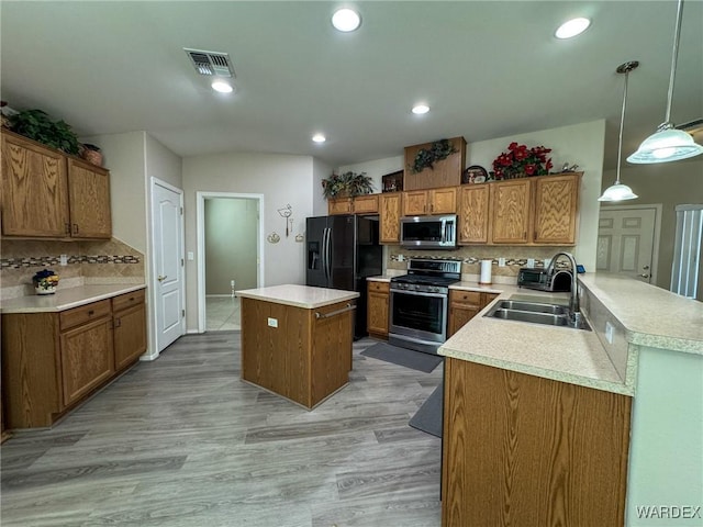 kitchen with decorative light fixtures, a peninsula, stainless steel appliances, light countertops, and a sink