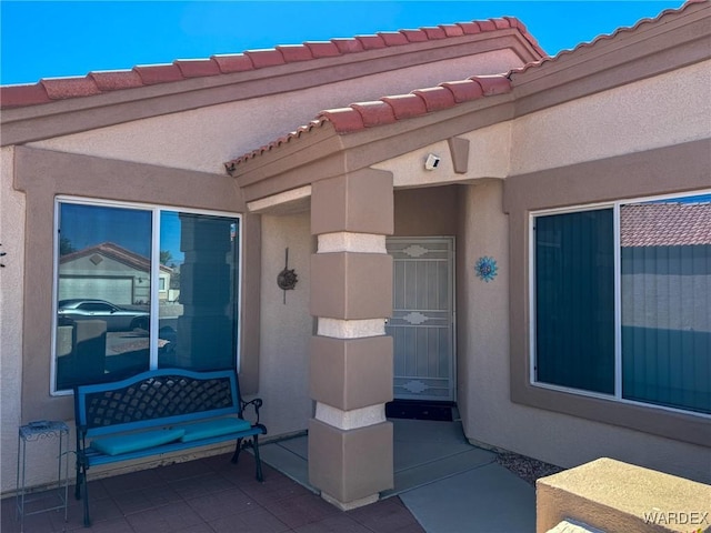 doorway to property with a tile roof, a patio, and stucco siding