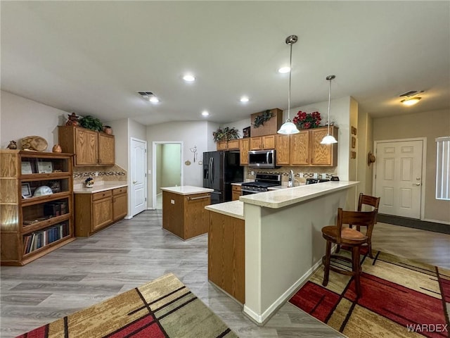 kitchen with brown cabinetry, appliances with stainless steel finishes, light countertops, and pendant lighting