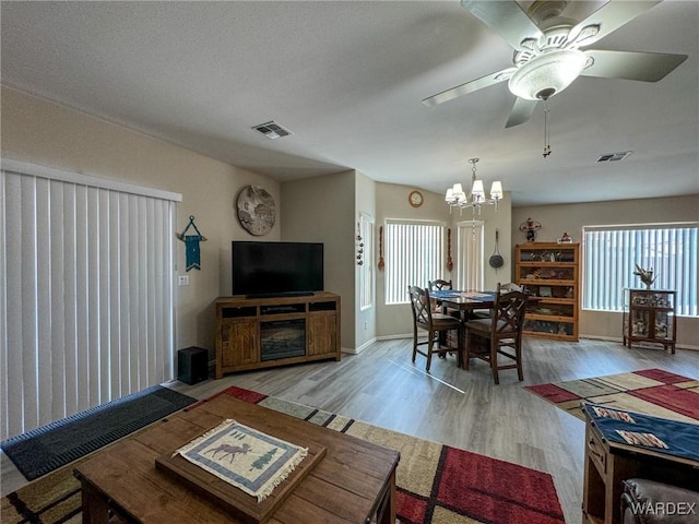 living area featuring light wood-type flooring, visible vents, baseboards, and ceiling fan with notable chandelier