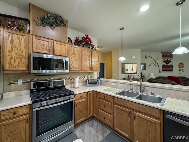 kitchen with a sink, stainless steel appliances, hanging light fixtures, and light countertops