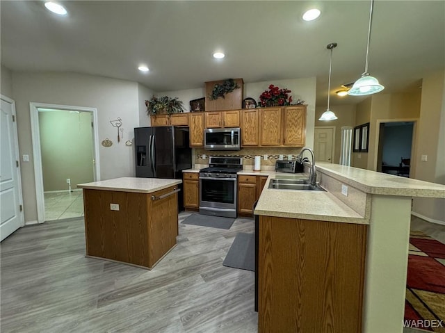 kitchen featuring pendant lighting, light countertops, appliances with stainless steel finishes, brown cabinetry, and a sink