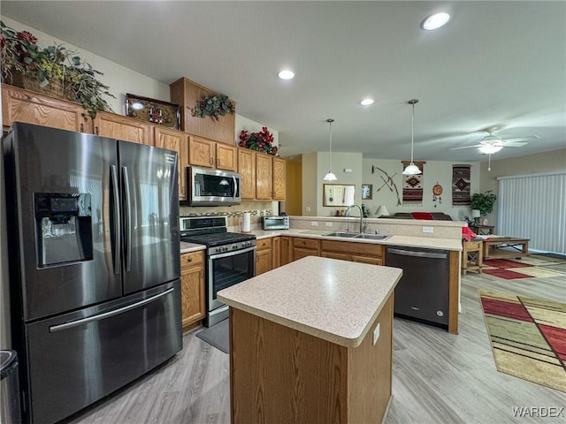 kitchen featuring a peninsula, a sink, light countertops, appliances with stainless steel finishes, and hanging light fixtures