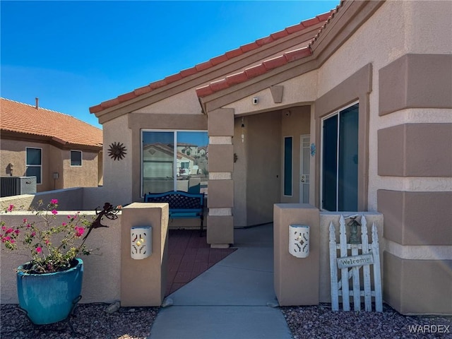 view of exterior entry with a tile roof, fence, and stucco siding