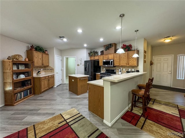 kitchen featuring brown cabinets, a peninsula, appliances with stainless steel finishes, and light countertops