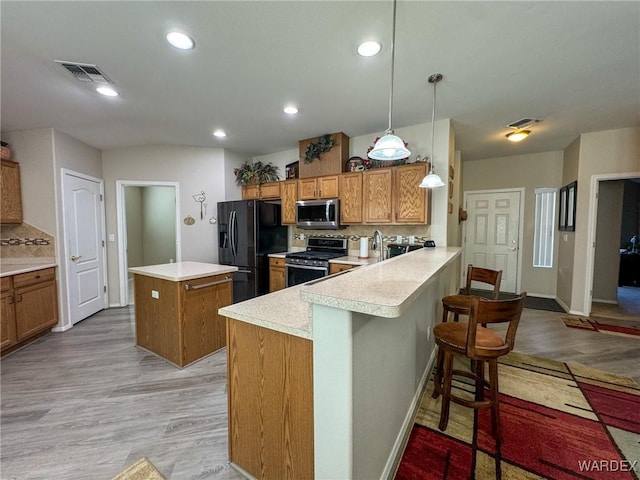 kitchen featuring pendant lighting, stainless steel appliances, light countertops, brown cabinetry, and a peninsula