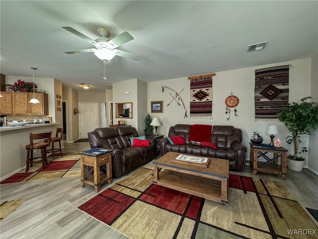 living room featuring a ceiling fan, visible vents, light wood-style flooring, and baseboards