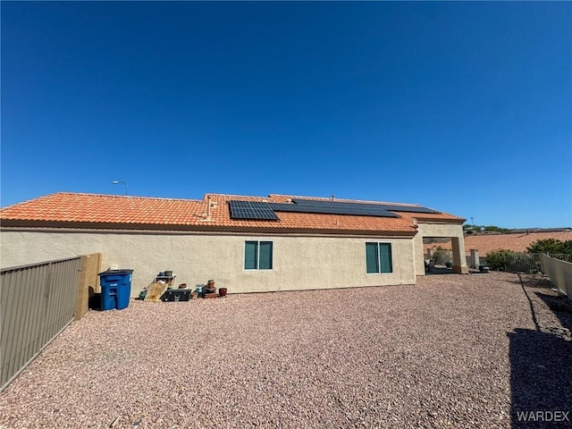 back of house with a tiled roof, stucco siding, fence, and roof mounted solar panels