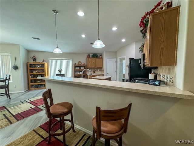 kitchen with pendant lighting, brown cabinets, a breakfast bar area, light countertops, and a peninsula