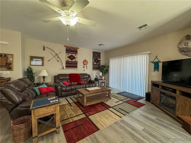 living room featuring light wood-type flooring, visible vents, and ceiling fan