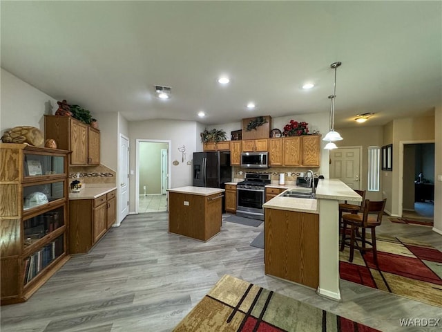 kitchen featuring stainless steel appliances, light countertops, decorative light fixtures, and an island with sink