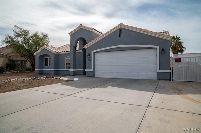 mediterranean / spanish-style house featuring an attached garage, a tile roof, concrete driveway, and stucco siding