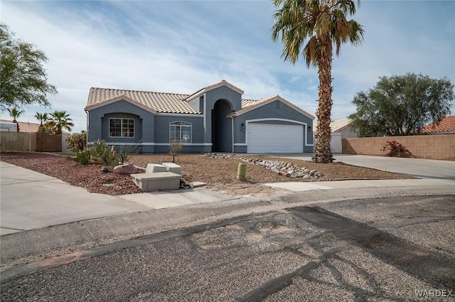 mediterranean / spanish house with a tile roof, stucco siding, concrete driveway, an attached garage, and fence