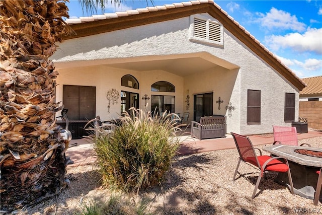 rear view of house featuring a patio, an outdoor fire pit, fence, a tile roof, and stucco siding