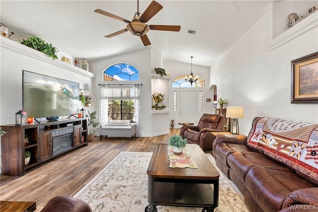 living room featuring arched walkways, high vaulted ceiling, ceiling fan with notable chandelier, wood finished floors, and visible vents