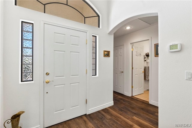 foyer entrance with arched walkways, dark wood-type flooring, and baseboards