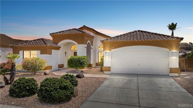 mediterranean / spanish home featuring a garage, concrete driveway, a tiled roof, and stucco siding