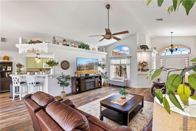 living area with ceiling fan with notable chandelier, high vaulted ceiling, light wood finished floors, and visible vents