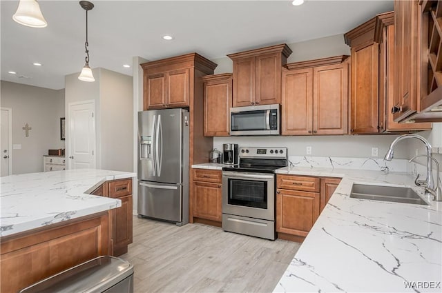 kitchen with light stone counters, stainless steel appliances, a sink, light wood-type flooring, and brown cabinets