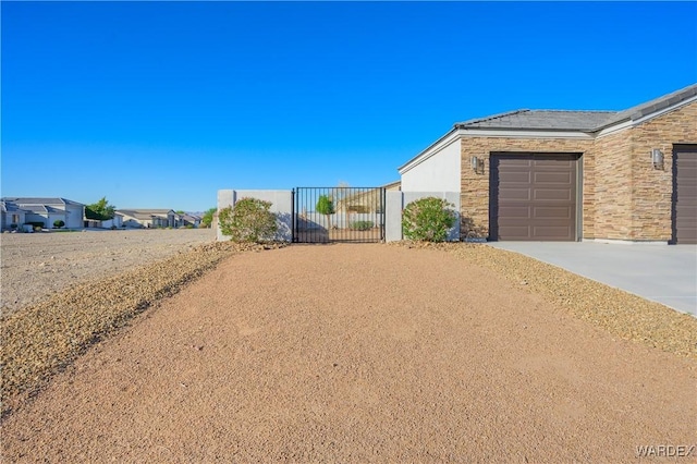 view of front facade featuring driveway, stone siding, and a gate