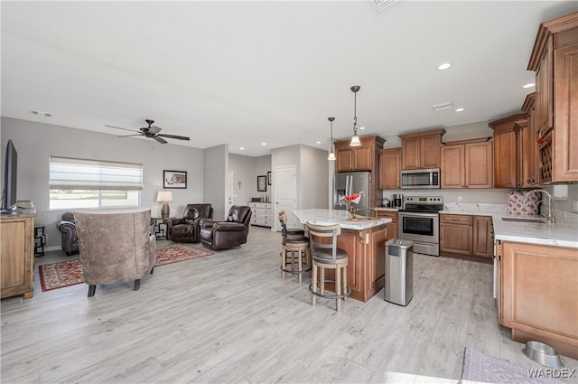 kitchen with light wood-style flooring, open floor plan, stainless steel appliances, a kitchen bar, and a sink