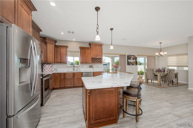 kitchen featuring brown cabinetry, light wood-style flooring, a kitchen island, stainless steel appliances, and a sink