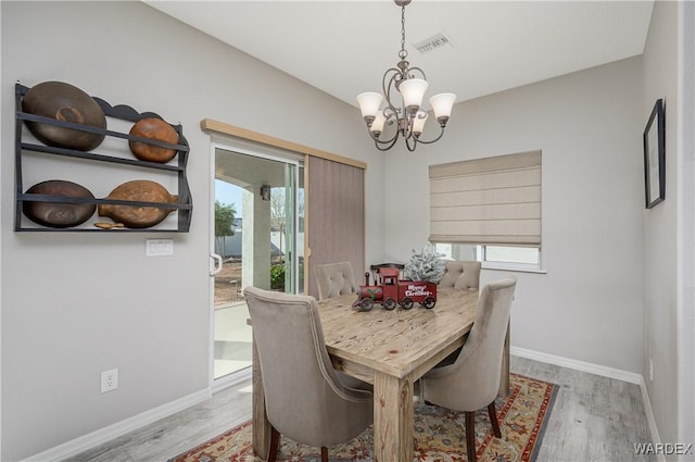 dining area with baseboards, light wood-style floors, visible vents, and an inviting chandelier