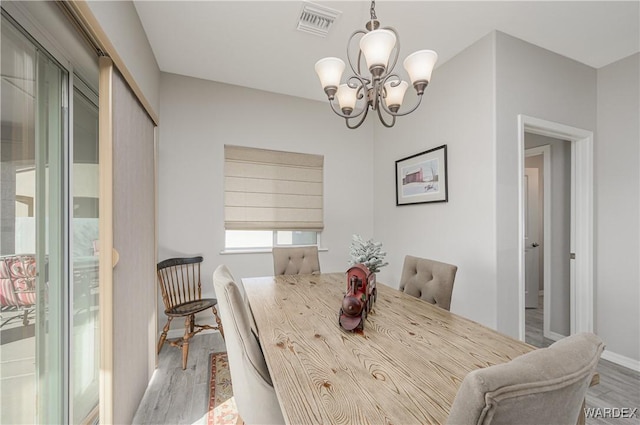 dining area featuring light wood-style floors, baseboards, visible vents, and a notable chandelier