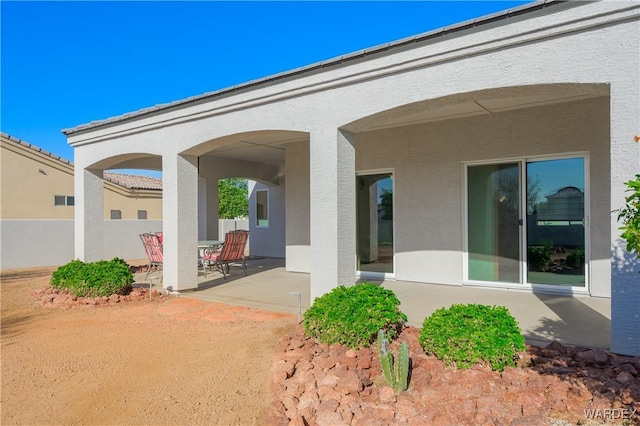 rear view of house with a patio area, fence, and stucco siding