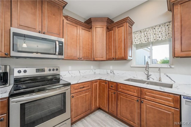 kitchen with light stone counters, stainless steel appliances, light wood-style flooring, brown cabinetry, and a sink