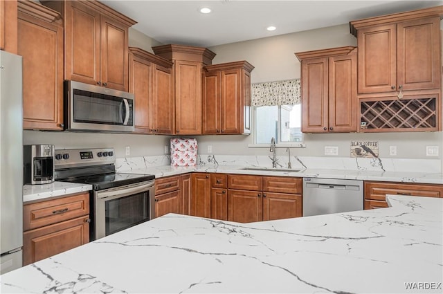 kitchen with light stone counters, brown cabinets, stainless steel appliances, a sink, and recessed lighting