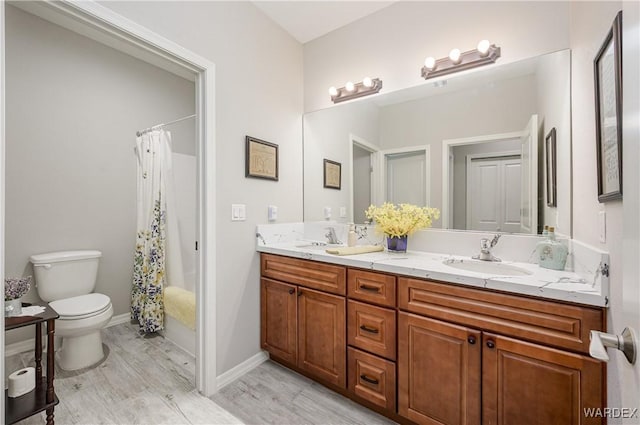 bathroom featuring toilet, wood finished floors, a sink, baseboards, and double vanity