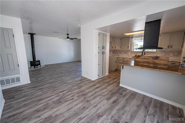 kitchen featuring visible vents, open floor plan, backsplash, range hood, and a wood stove