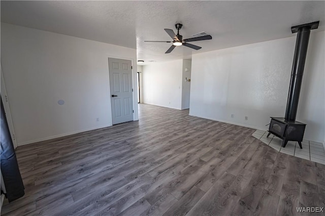 unfurnished living room featuring a textured ceiling, a ceiling fan, baseboards, dark wood-style floors, and a wood stove