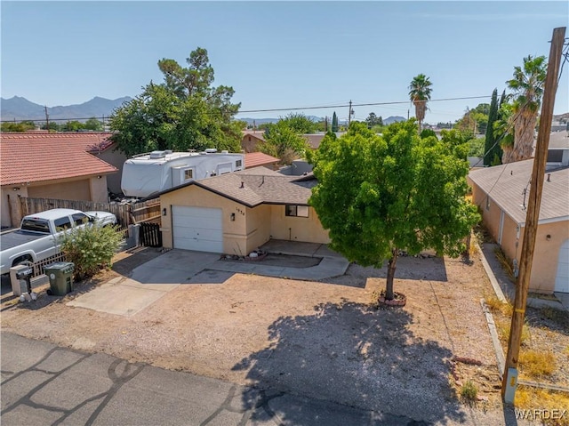 view of front of home featuring concrete driveway, an attached garage, fence, a mountain view, and stucco siding