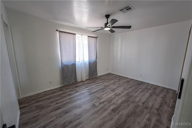 empty room with ceiling fan, dark wood-type flooring, visible vents, and baseboards