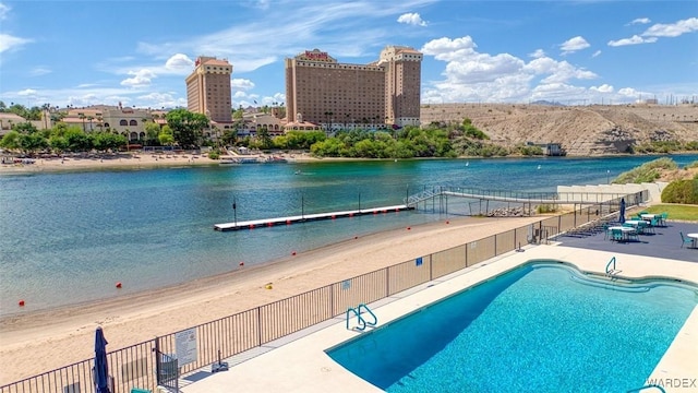 pool featuring a patio, a water view, and fence