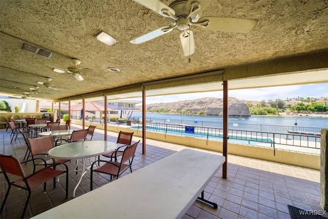 view of patio with a ceiling fan, visible vents, fence, and a water view