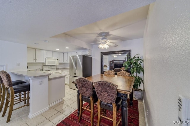 kitchen featuring white appliances, a peninsula, a ceiling fan, white cabinetry, and light tile patterned floors