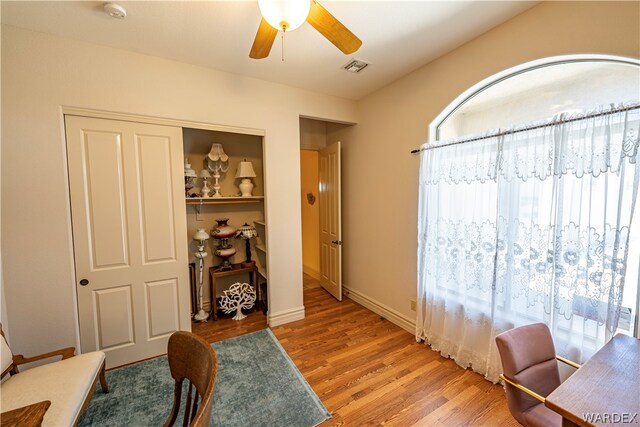 home office with a ceiling fan, visible vents, baseboards, and wood finished floors