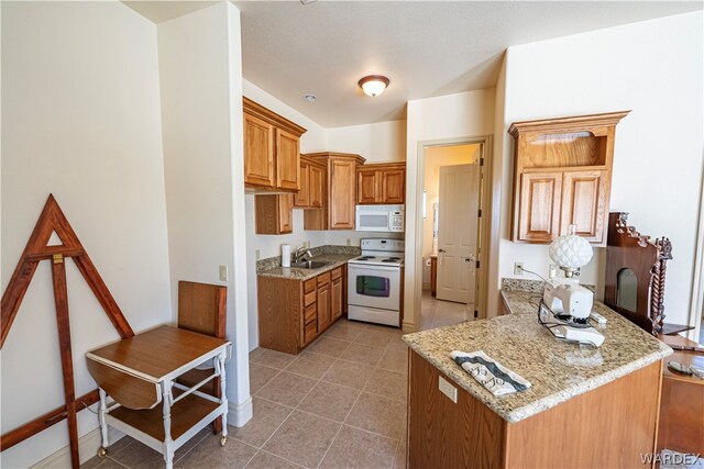 kitchen featuring white appliances, light tile patterned floors, brown cabinetry, light stone countertops, and a sink