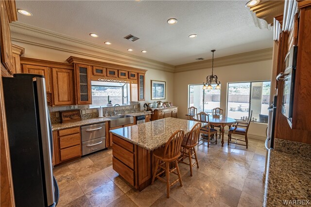 kitchen with stainless steel appliances, a healthy amount of sunlight, brown cabinets, a center island, and glass insert cabinets