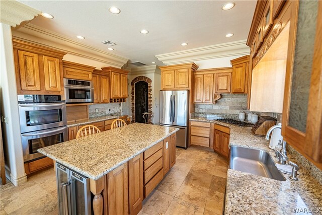 kitchen with appliances with stainless steel finishes, a kitchen island, light stone counters, and a sink