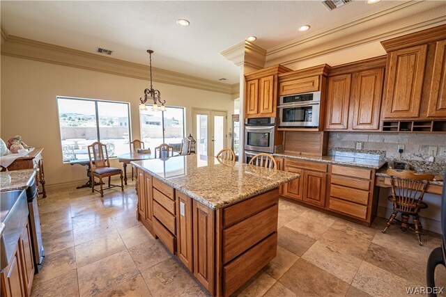 kitchen featuring light stone counters, a center island, brown cabinets, visible vents, and hanging light fixtures